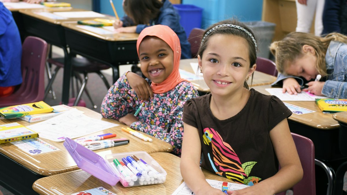 Two students smile while working at their desks