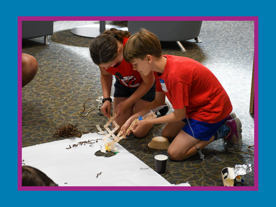 Two students testing a homemade invention of popsicle sticks, syringes, and household items.