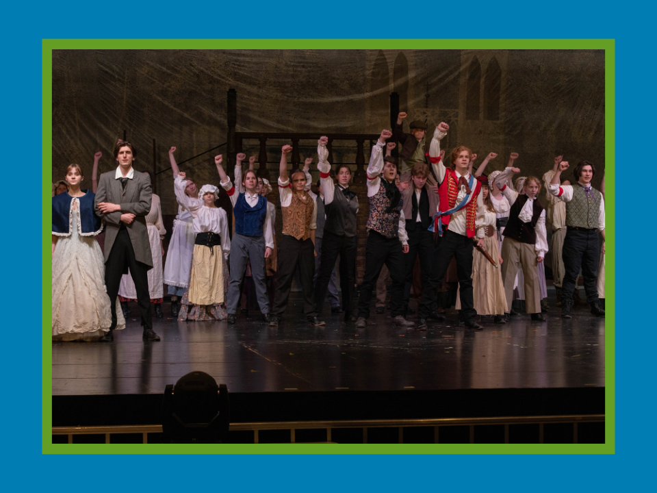 Cast of Les Mis raise their right arm in the air during a scene on stage.