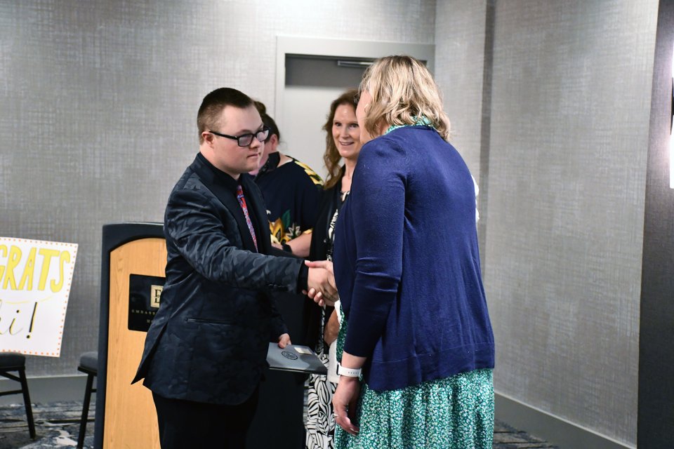 Adult student in suit coat and glasses receiving completion certificate
