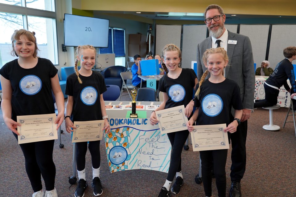Four girls with the superintendent holding certificates awarded for winning Battle of the Books