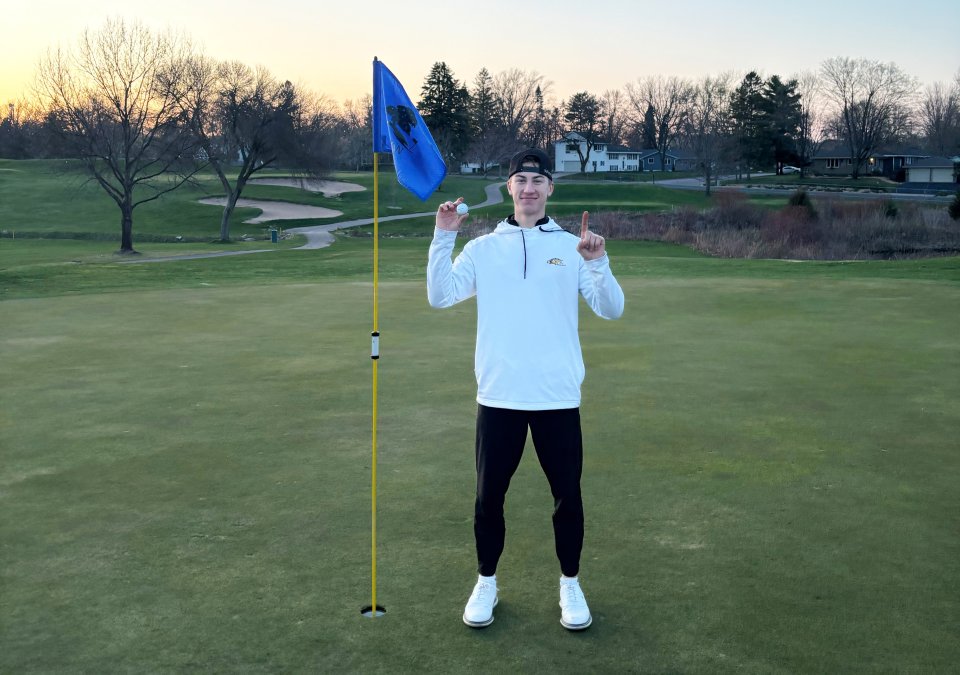 Ryan Kardell holding golf ball and holding up one finger to signify a hole-in-one