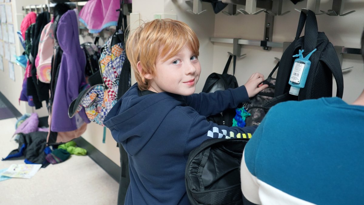 boy putting backpack on hook