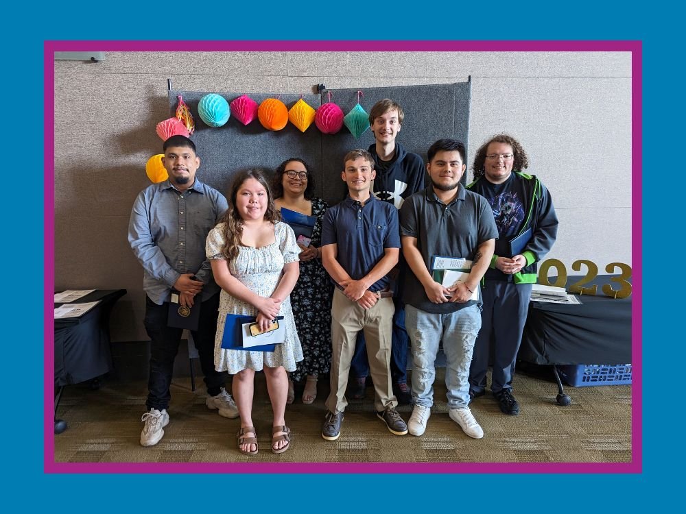 seven students standing against backdrop with diplomas