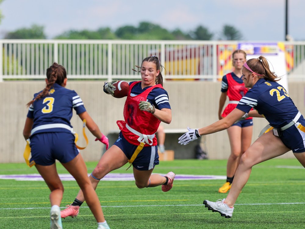 girl playing flag football avoiding other players while running with the ball