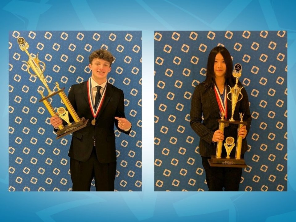Two students wearing suit coats and medals while holding trophies